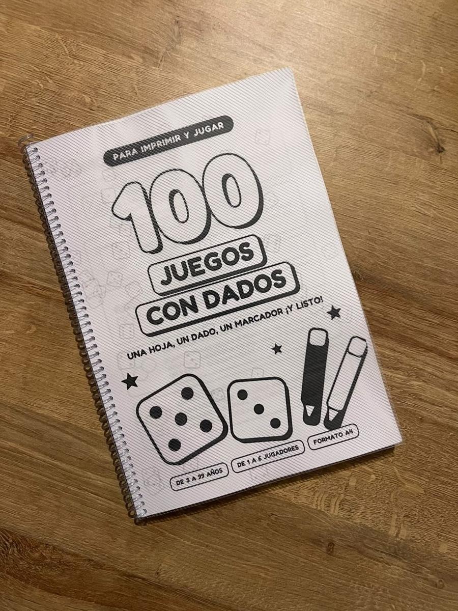 Tapa del libro 100 juegos con dados impreso y anillado sobre una mesa de madera